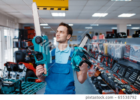 Worker holds big and small chainsaws in tool store Worker holds big and small chainsaws in tool store 65538792