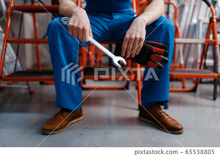 Male employee in uniform holds wrench, tool store 65538805
