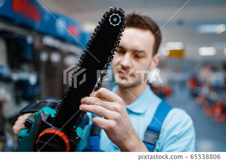 Worker in uniform holds electric saw in tool store Worker in uniform holds electric saw in tool store 65538806