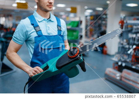 Worker in uniform holds electric saw in tool store Worker in uniform holds electric saw in tool store 65538807