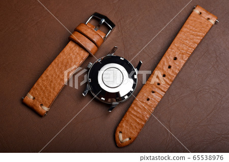 Vintage wristwatch on a brown leather background. Classic watch straps. 65538976