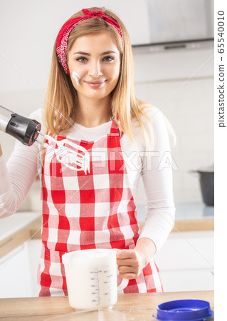 Beautiful girl with a hand whisk smiles at camera 65540010