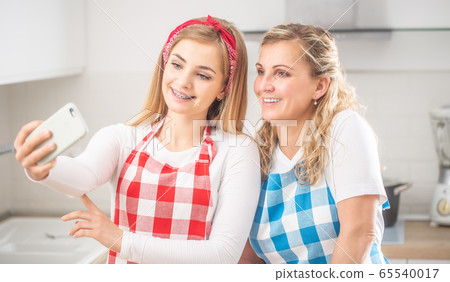 Mother and daughter wearing aprons take a selfie 65540017