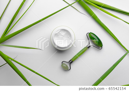 Face moisturizer cream with jade massager on white background, healthy lifestyle without surgery 65542154