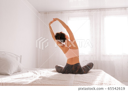 Back view of slim woman doing yoga in white bedroom. Stay home concept. Back view of slim woman doing yoga in white bedroom. Stay home concept. 65542619