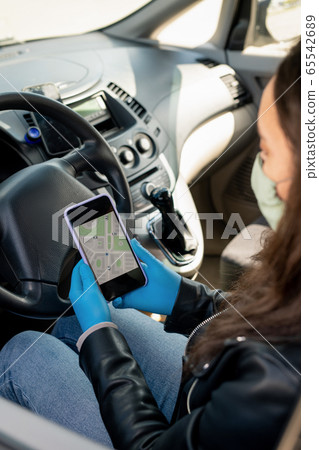 Female taxi driver in protective gloves looking at navigator map in smartphone 65542689