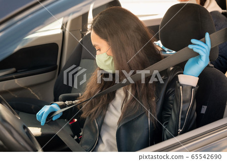 Young brunette female in leather jacket, gloves and mask fastening seatbelt 65542690