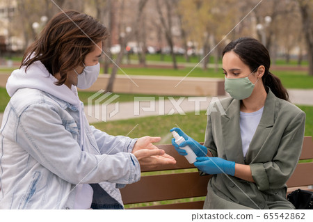 Young female in protective gloves and mask spraying sanitizer on hands of man Young female in protective gloves and mask spraying sanitizer on hands of man 65542862