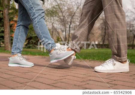 Legs of young man and woman in pants and sports shoes making foot bump 65542906