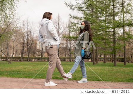 Pretty young woman and her boyfriend in masks and casualwear stretching legs 65542911