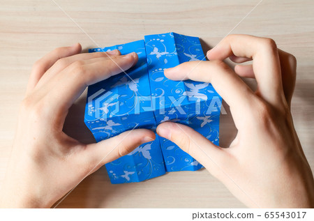 Girl's hands making origami blue dress from butterfly printed paper. Step by step instruction, step 9. Mother's day, birhday, summer gift, family leisure time concept. DIY tutorial, flatlay, top view 65543017