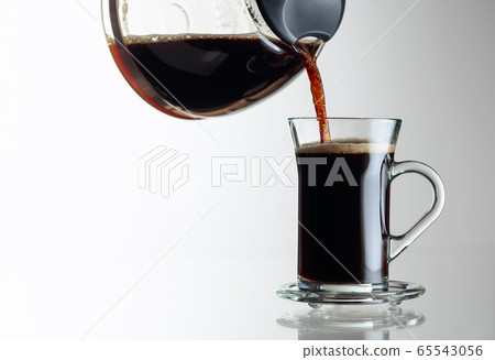 Coffee is poured from the coffee maker into a cup. 65543056