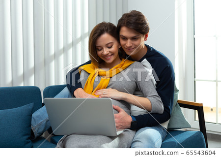 Mirthful pregnant couple at home with modern gadget 65543604