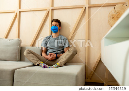 Young man in blue mask sitting on sofa in room Young man in blue mask sitting on sofa in room 65544819