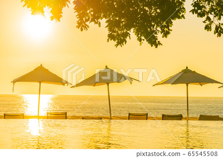 Beautiful tropical outdoor beach sea ocean with umbrella and chiar around outdoor swimming pool at sunset or sunrise time 65545508