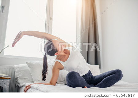 slender sporty woman doing exercises on bed at home 65545617