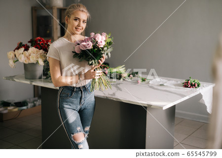 Smiling young woman wearing fashion clothes holding bouquet of flowers 65545799