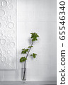 White brick wall with a white artwork and a green branch in a glass vase 65546340