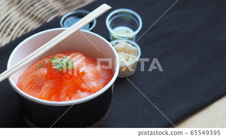 Side view of Salmon with Japanese rice or Salmon Ikura Don in paper dish from delivery restaurant on black Table cloths Side view of Salmon with Japanese rice or Salmon Ikura Don in paper dish from delivery restaurant on black Table cloths 65549395