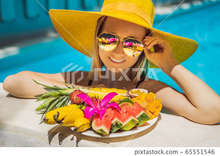 Young woman relaxing and eating fruit plate by the hotel pool. Exotic summer diet. Photo of legs Young woman relaxing and eating fruit plate by the hotel pool. Exotic summer diet. Photo of legs 65551546