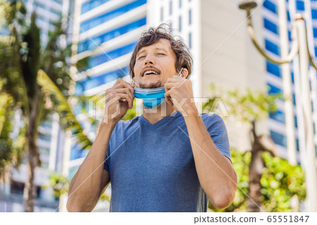 Quarantine is over concept. Man taking off mask against the background of small town houses. We are Quarantine is over concept. Man taking off mask against the background of small town houses. We are 65551847