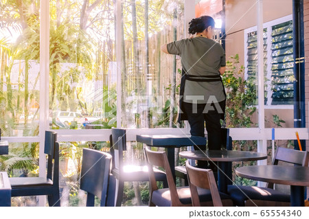 Back view of maid closes the glass window to turn on the air conditioner in the coffee shop Back view of maid closes the glass window to turn on the air conditioner in the coffee shop 65554340