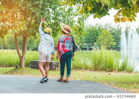 Back view of happiness female friends walking together beside the fountain in the public park. 65554668