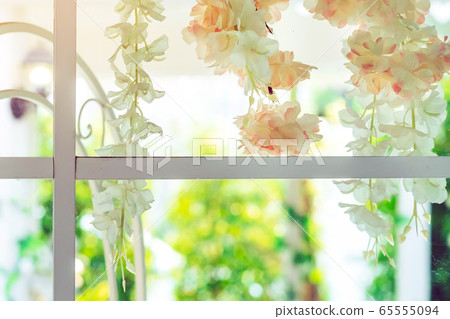 Beautiful artificial flowers hung on glass windows to decorate for a garden party. View from the window on the glass. 65555094