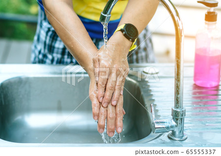 A woman washing hands from the tap with pink soap in a aluminium tub. Concepts of Flu virus, Covid-19 (Coronavirus disease). Selective focus. A woman washing hands from the tap with pink soap in a aluminium tub. Concepts of Flu virus, Covid-19 (Coronavirus disease). Selective focus. 65555337