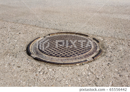 old metal sewer manhole cover in asphalt 65556442