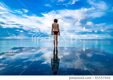 Sky and sea of the Maldives Reflection of a woman in a swimsuit standing in the infinity pool 65557450