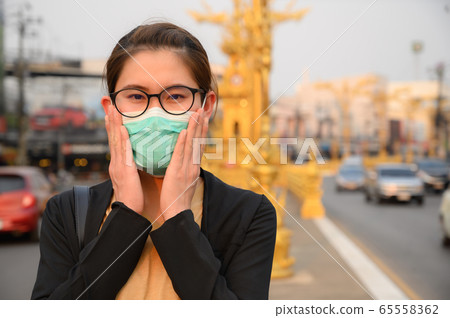 Woman wearing surgical mask for protect bad air pollution or virus in pandemic situations. Conceptual of urban lifestyle and using mask for avoid bad environment. 65558362