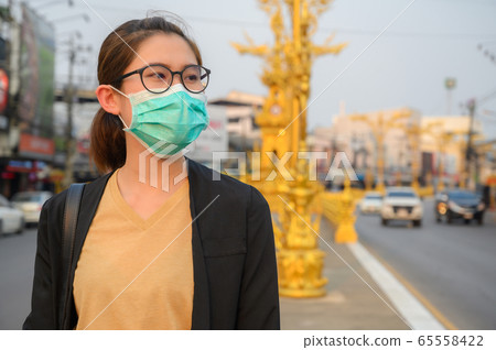 Woman wearing surgical mask for protect bad air pollution or virus in pandemic situations. Conceptual of urban lifestyle and using mask for avoid bad environment. 65558422