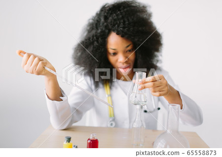 Portrait of a young beautiful African American girl researcher chemistry student carrying out research in a chemistry lab. Scientist analyzing a test-tube. Portrait of a young beautiful African American girl researcher chemistry student carrying out research in a chemistry lab. Scientist analyzing a test-tube. 65558873