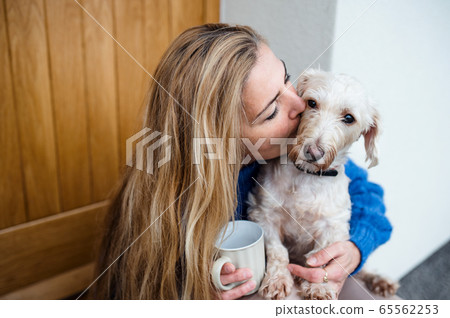Mature woman relaxing outdoors by front door at home with coffee and pet dog. 65562253