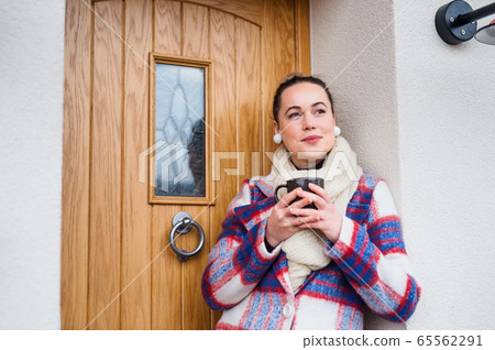 Young woman relaxing outdoors by front door at home, holding cup of coffee. Young woman relaxing outdoors by front door at home, holding cup of coffee. 65562291