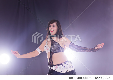 Young woman belly dancer in exotic dress with gold, dancing tribal fusion dance in studio. Young woman belly dancer in exotic dress with gold, dancing tribal fusion dance in studio. 65562292