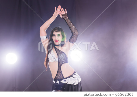 Young woman belly dancer in exotic dress with gold, dancing tribal fusion dance in studio. Copy space. Young woman belly dancer in exotic dress with gold, dancing tribal fusion dance in studio. Copy space. 65562305
