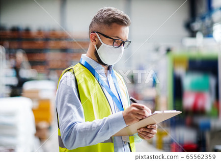 Technician or engineer with protective mask working in industrial factory, writing. Technician or engineer with protective mask working in industrial factory, writing. 65562359
