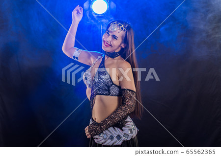 Young woman belly dancer in exotic dress with gold, dancing tribal fusion dance in studio. Young woman belly dancer in exotic dress with gold, dancing tribal fusion dance in studio. 65562365