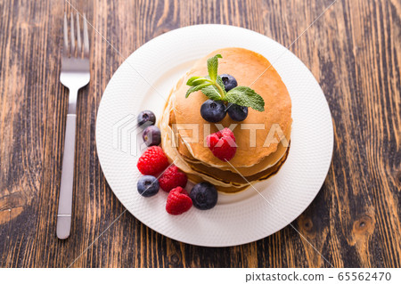 Homemade sweet pancakes with blueberries and raspberries on a white plate, top view. 65562470