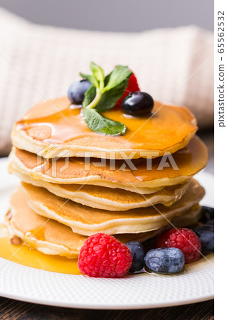 Pile of pancakes with blueberries and raspberries and maple syrup for breakfast on wooden table. Pile of pancakes with blueberries and raspberries and maple syrup for breakfast on wooden table. 65562532