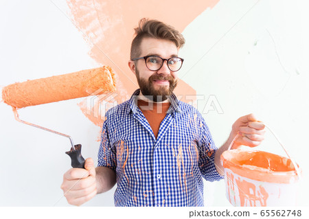 Funny man painting interior wall of home with paint roller. Redecoration, renovation, apartment repair and refreshment concept. Funny man painting interior wall of home with paint roller. Redecoration, renovation, apartment repair and refreshment concept. 65562748