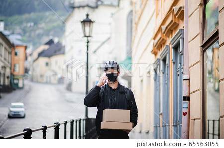 Delivery man courier with face mask and smartphone delivering parcel box in town. 65563055