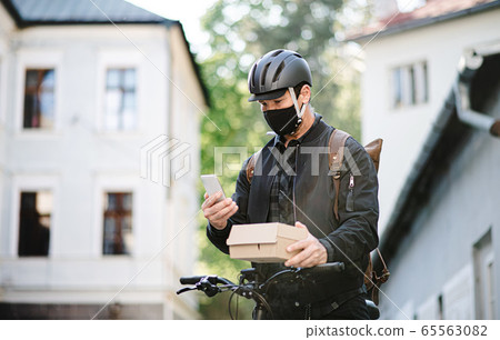 Delivery man courier with face mask and bicycle using smartphone in town. 65563082