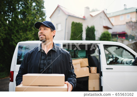 Front view of delivery man courier delivering parcel box in town. Front view of delivery man courier delivering parcel box in town. 65563102