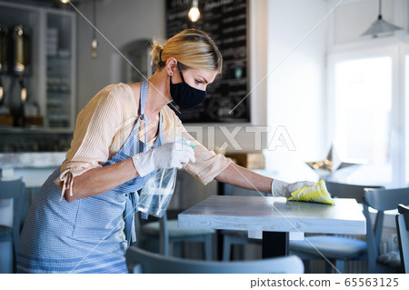 Coffee shop woman owner working with face mask and gloves, disinfecting tables. 65563125