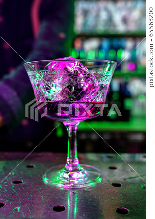 Close up of alcoholic cocktail, beverage, drink, prepared by professional barman in multicolored neon light 65563200
