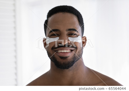 Portrait of smiling biracial man use under eye patches 65564044