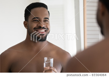 Smiling biracial young man drinking water in bathroom 65564064